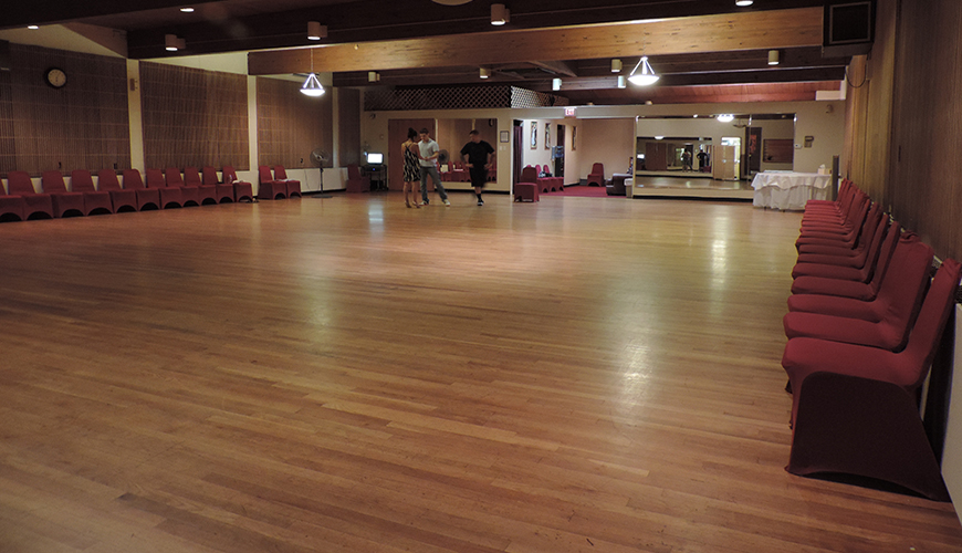 An elegant ballroom dance studio with one couple taking a lesson from an instructor.