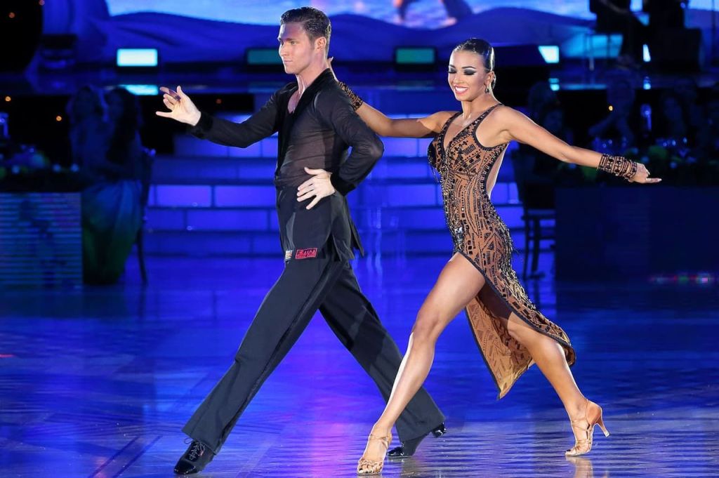 Latin champion ballroom dancers striding across the floor in a side-by-side position.